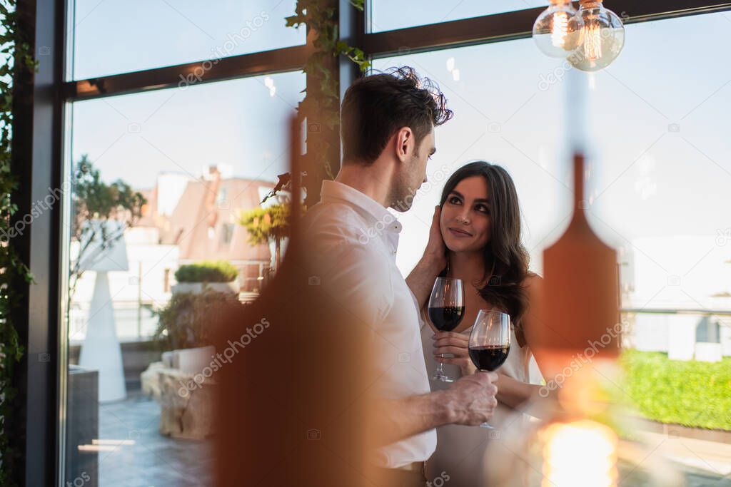 cheerful woman holding glass of wine and looking at man in restaurant 