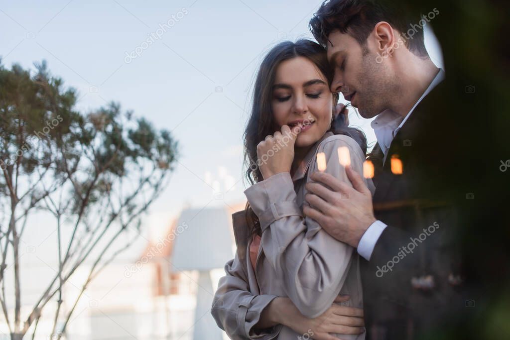 man hugging woman on terrace behind blurred window of restaurant 