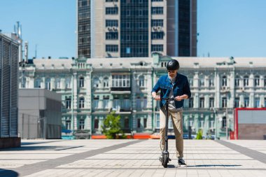 full length of man in sunglasses and helmet riding e-scooter in urban city 