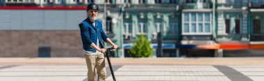 mature man in sunglasses and helmet riding e-scooter in urban city, banner