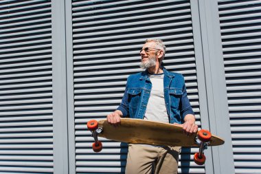 positive and middle aged man in sunglasses holding longboard 