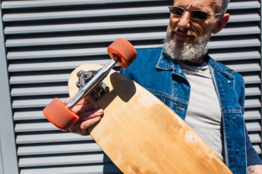 smiling and middle aged man in sunglasses holding longboard 