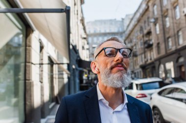bearded and mature man listening music in earphones outside