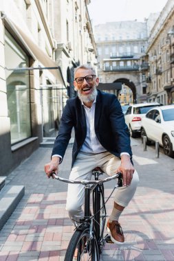 joyful mature man listening music in earphones and riding bicycle 