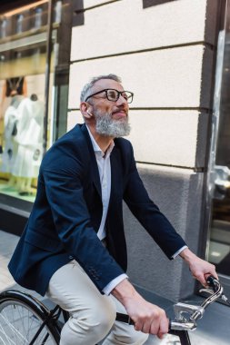 pleased mature man listening music in earphones and riding bicycle 