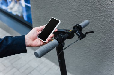 cropped view of mature businessman holding smartphone with blank screen near e-scooter