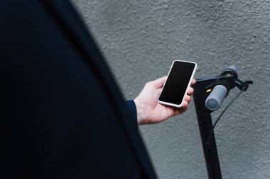 partial view of mature man holding smartphone with blank screen near e-scooter