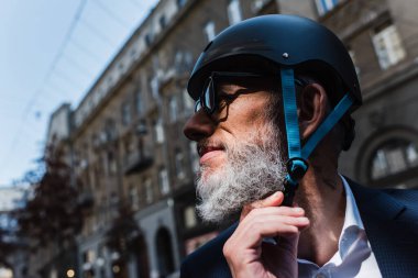 smiling and mature businessman adjusting helmet outside