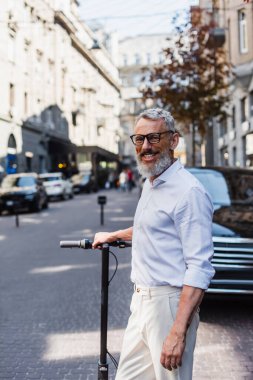 smiling middle aged man in white shirt near electric scooter on street 