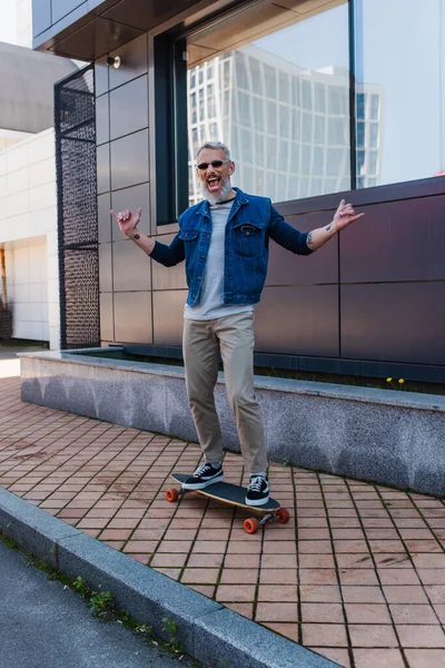Full Length Excited Man Open Mouth Riding Longboard Showing Rock — Stock Photo, Image
