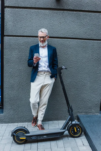 Щасливий Зрілий Бізнесмен Блейзері Стоїть Біля Електронного Скутера Використовує Смартфон — стокове фото