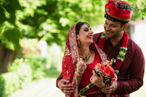 happy indian married couple in traditional wedding clothes looking at each other outside