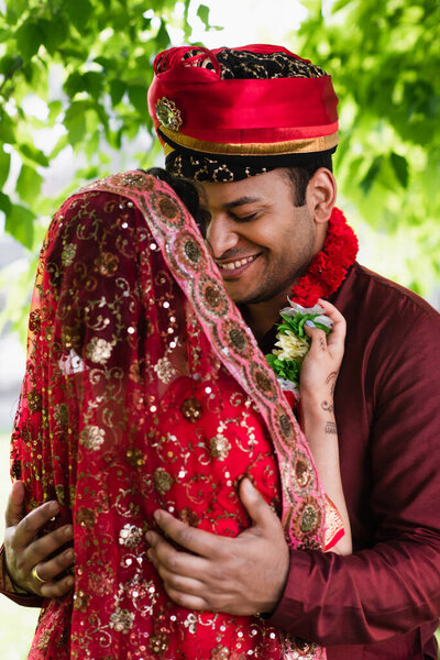 Индийская невеста в платке в цветочной гирлянде на счастливом женихе 