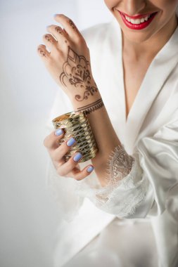 cropped view of happy indian woman with mehndi on hand wearing bracelet on grey clipart