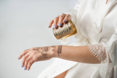 cropped view of indian woman with mehndi on hand wearing bracelet while getting ready to wedding isolated on white clipart