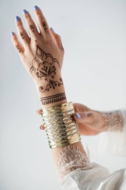 cropped view of indian woman with mehndi on hands wearing golden bracelet while getting ready to wedding isolated on white clipart