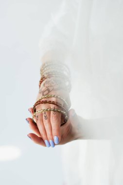 cropped view of young indian bride with mehndi wearing bracelets on white  clipart