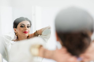 Hintli gelin kolye takıyor ve beyaz aynaya bakıyor.