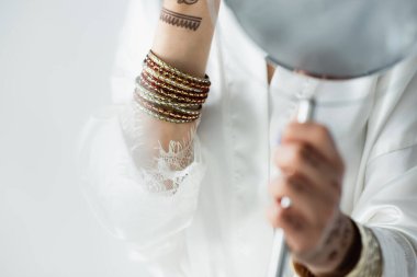 cropped view of indian bride with mehndi holding mirror on white clipart