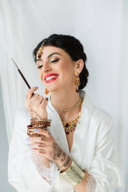 Memnun Hintli gelin mehndi ile beyaz üzerinde kozmetik fırça tutuyor 