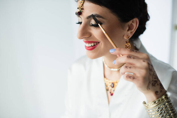 счастливая индийская невеста с бровями в стиле mehndi с косметической щеткой на белом 
