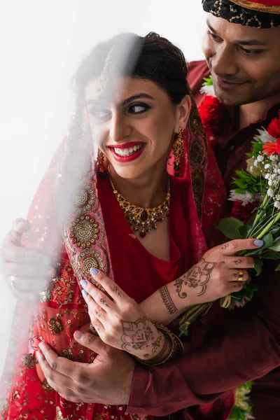 Sarıklı mutlu Hintli adam gülümseyen geline sarılıyor mehndi beyaz çiçeklerle sarılıyor.