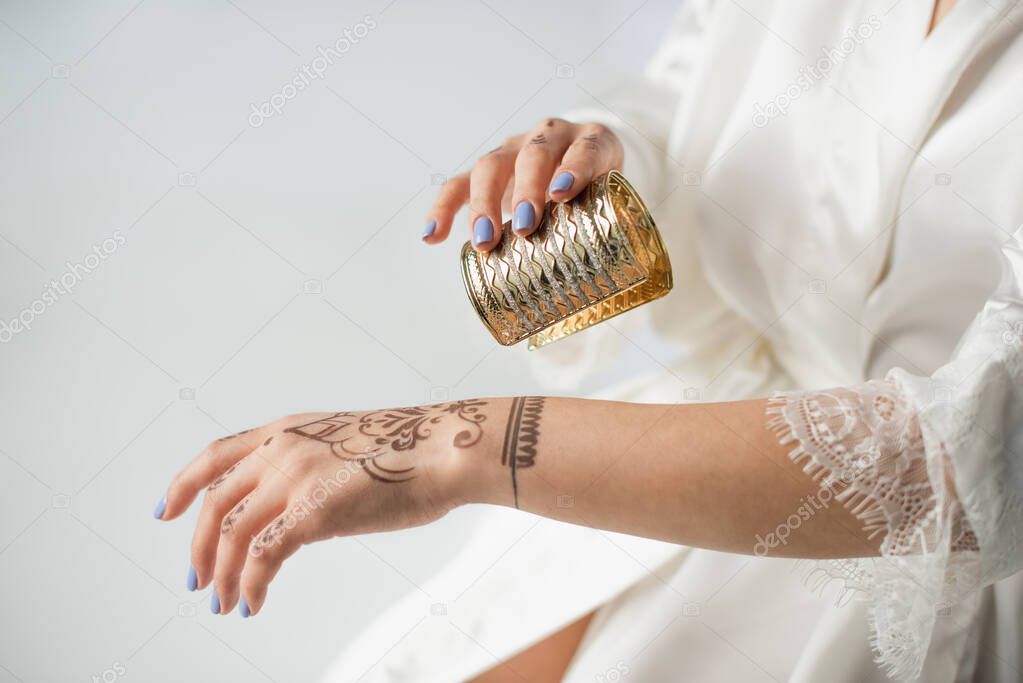 cropped view of indian woman with mehndi on hand wearing bracelet while getting ready to wedding isolated on white