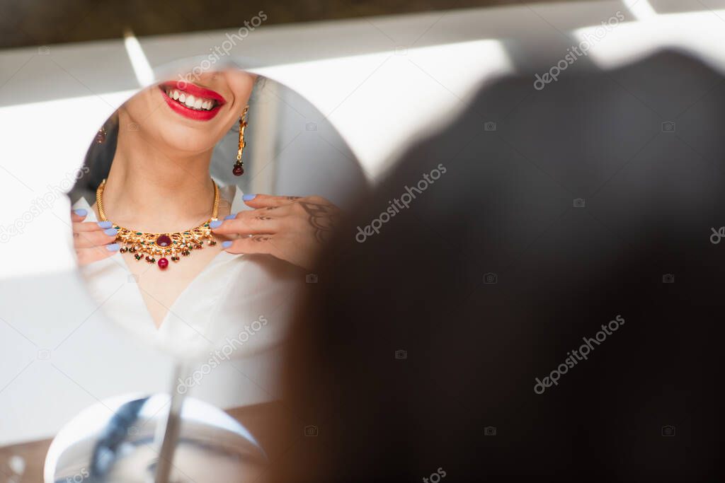 cropped view of happy indian bride wearing necklace near mirror