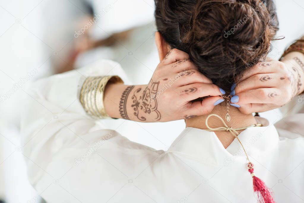 Back view of indian bride with mehndi on hands wearing necklace