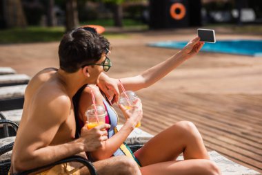 Portakal suyu içen genç çift oteldeki akıllı telefondan selfie çekiyor. 