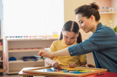 Genç öğretmen ve Asyalı kız Montessori okulunda dünya haritası bulmacasını birleştiriyor.