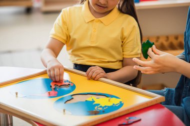 Montessori okulundaki öğretmenin yanında dünya haritasını birleştiren bir kızın görüntüsü.