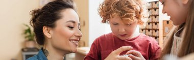 Kıvırcık oğlanın yanında mutlu öğretmen ve Montessori okulundaki bulanık kız, afiş.