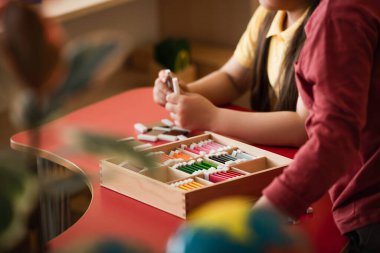 Montessori okulunda, bulanık ön planda çocukların eğitim oyunu oynamalarına dair kırpık bir bakış açısı