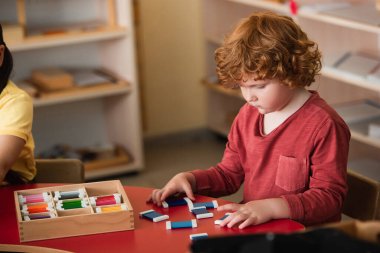 curly boy sorting colorful cards near girl in montessori school clipart