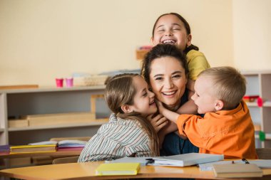 Çok mutlu çoklu etnik çocuklar Montessori okulunda mutlu öğretmeni kucaklıyor.