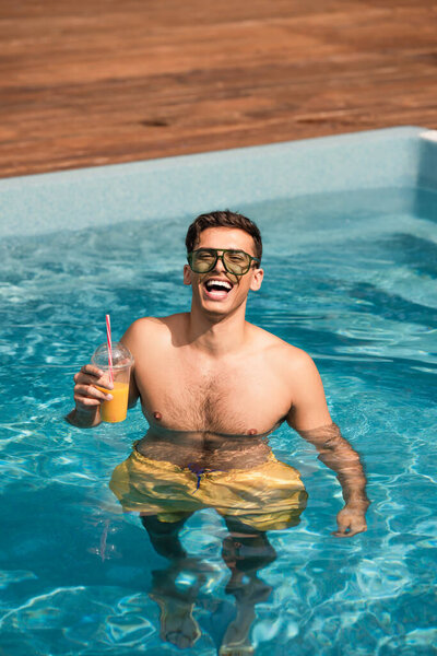 Веселый мужчина с апельсиновым соком в бассейне 