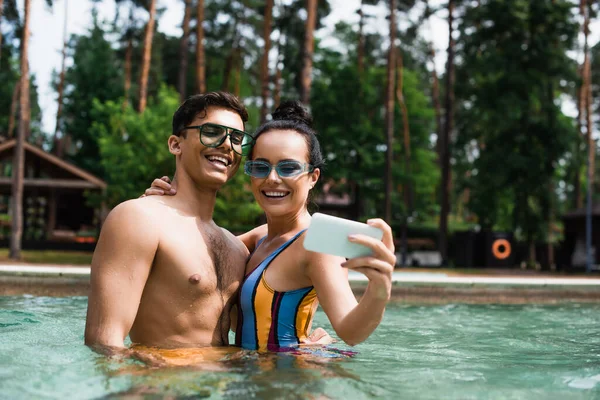 Mulher Sorridente Abraçando Namorado Enquanto Toma Selfie Piscina Resort — Fotografia de Stock