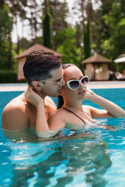 Sexy man kissing girlfriend in sunglasses in swimming pool 