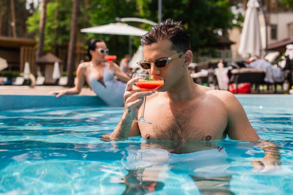 Young man drinking cocktail in swimming pool on resort 