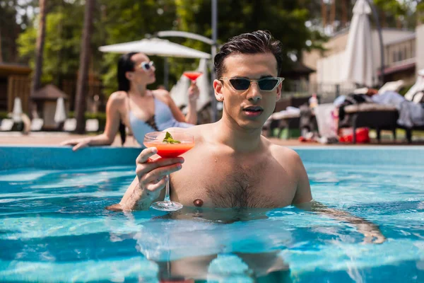 Man Wet Hair Holding Cocktail Swimming Pool Blurred Girlfriend — Stock Photo, Image