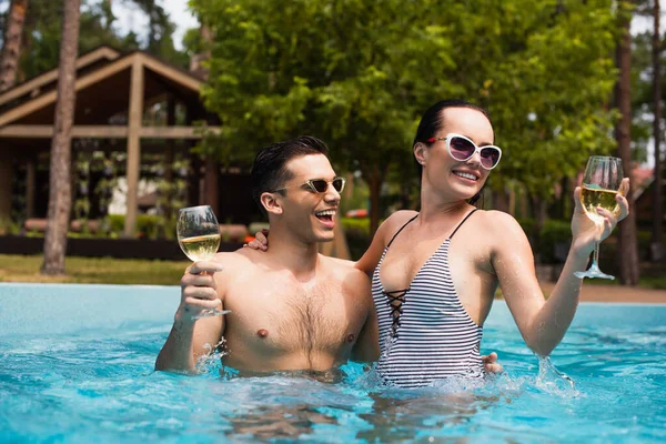 女性でストライプ水着保持ワインと抱擁男でプール — ストック写真