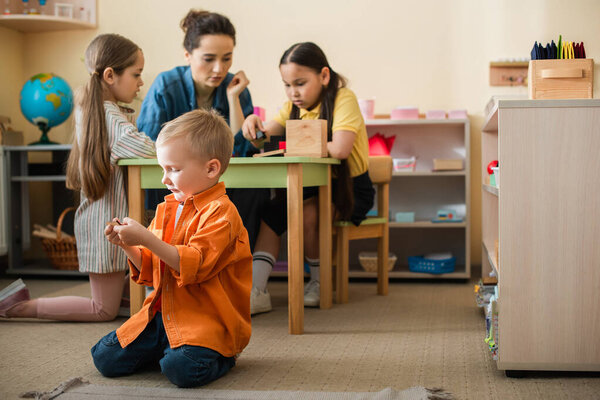 boy playing on floor near interracial girls and teacher on blurred background