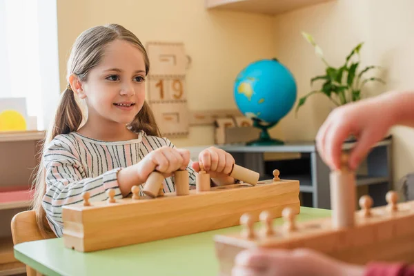 Uśmiechnięta Dziewczyna Gra Edukacyjna Elementami Drewnianymi Pobliżu Zamazanego Chłopca — Zdjęcie stockowe