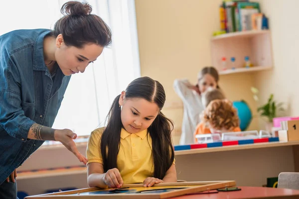 Nauczyciel Wskazując Puzzle Pobliżu Azjatyckiej Dziewczyny Szkole Montessori — Zdjęcie stockowe