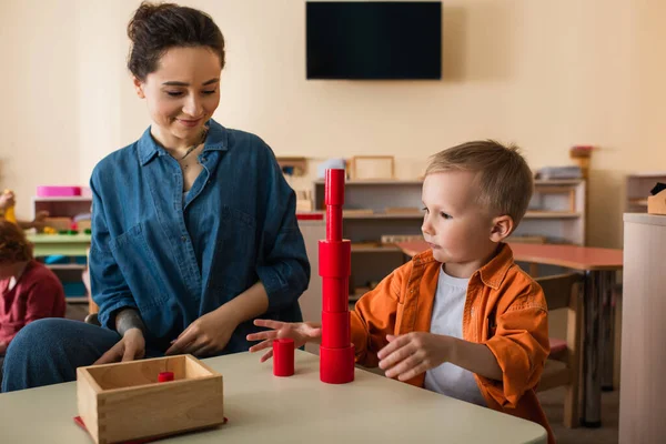 Profesor Sonriente Mirando Niño Haciendo Torre Cilindros Madera Roja — Foto de Stock