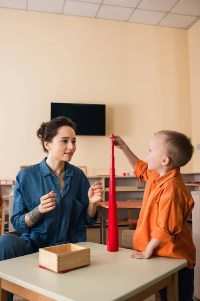 Niño Haciendo Torre Cilindros Rojos Cerca Profesor Joven Escuela Montessori — Foto de Stock