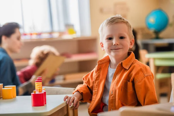 Happy Boy Looking Camera Red Yellow Wooden Blocks Teacher Blurred — Stock Photo, Image