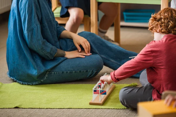 Chłopiec Gra Małymi Flagami Międzynarodowymi Podłodze Pobliżu Nauczyciela Szkole Montessori — Zdjęcie stockowe