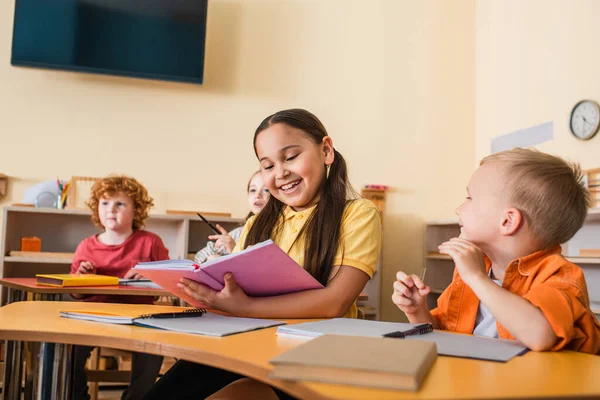 Szczęśliwy Azji Dziewczyna Czytanie Książki Pobliżu Przyjaciół Podczas Lekcji Montessori — Zdjęcie stockowe